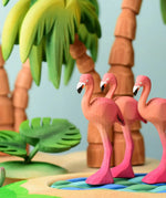 Play scene showing Bumbu toys handcrafted wooden flamingo figures on a pond and palm tree figures in the background