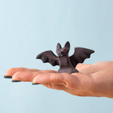 An adult hand holding the Bumbu handmade and hand painted wooden standing bat figure available at Babipur showing its size