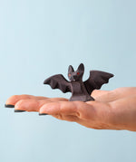 An adult hand holding the Bumbu handmade and hand painted wooden standing bat figure available at Babipur showing its size