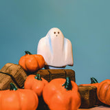A wooden Bumbu ghost figure placed on wooden hay bales surrounded by wooden pumpkin figures.
