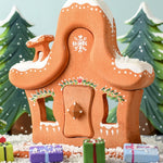 A Christmas scene with the Bumbu gingerbread house and Christmas presents outside the house and the trees in the background