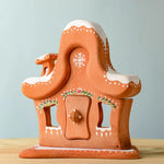 A wooden Bumbu gingerbread house with white hand painted snow and holy above the door and windows