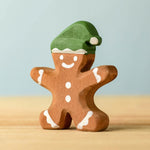 A wooden Bumbu gingerbread cookie boy with hand painted white detailing and wearing a green hat