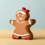 A wooden Bumbu gingerbread cookie girl with hand painted white detailing wearing a red bow on her head 
