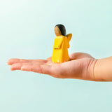 Adult hand holding a Bumbu wooden golden fairy figure showing scale