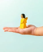 Adult hand holding a Bumbu wooden golden fairy figure showing scale