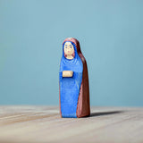 Bumbu Handmade Wooden Mary Figure kneeling down on a wooden table with a blue background.