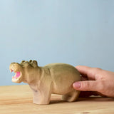 Adult hand holding a Bumbu toys handcrafted wooden grey standing hippo figure showing scale