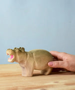 Adult hand holding a Bumbu toys handcrafted wooden grey standing hippo figure showing scale