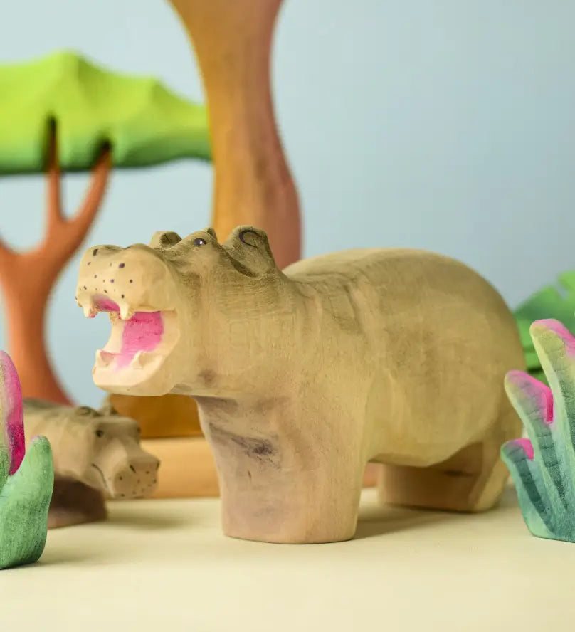 Bumbu toys handcrafted wooden grey standing hippo figure in a playscene with trees in the background