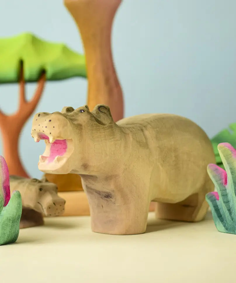 Bumbu toys handcrafted wooden grey standing hippo figure in a playscene with trees in the background