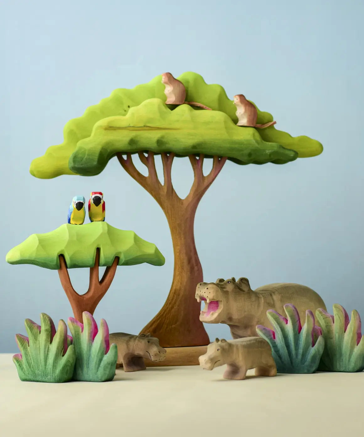 A playscene using Bumbu toys handcrafted wooden trees, grass, monkey, parrots and hippo animal figures