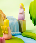A playscene showing a Bumbu handcrafted wooden lavender fairy figure on top of rocks and a small waterfall