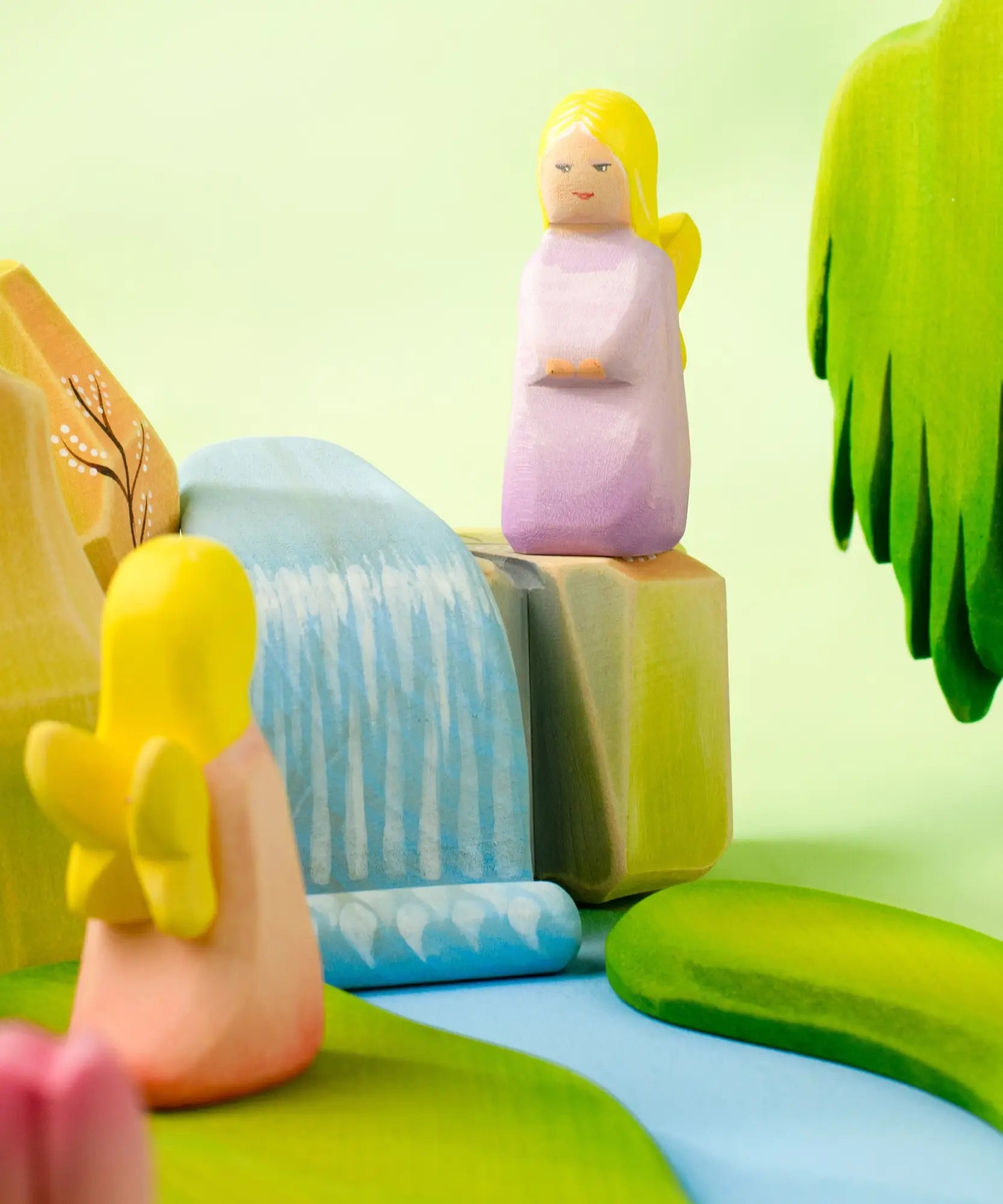 A playscene showing a Bumbu handcrafted wooden lavender fairy figure on top of rocks and a small waterfall