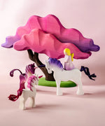 Bumbu wooden pink fairy figure standing on top of a white unicorn next to small pink unicorns and blossom tree figures