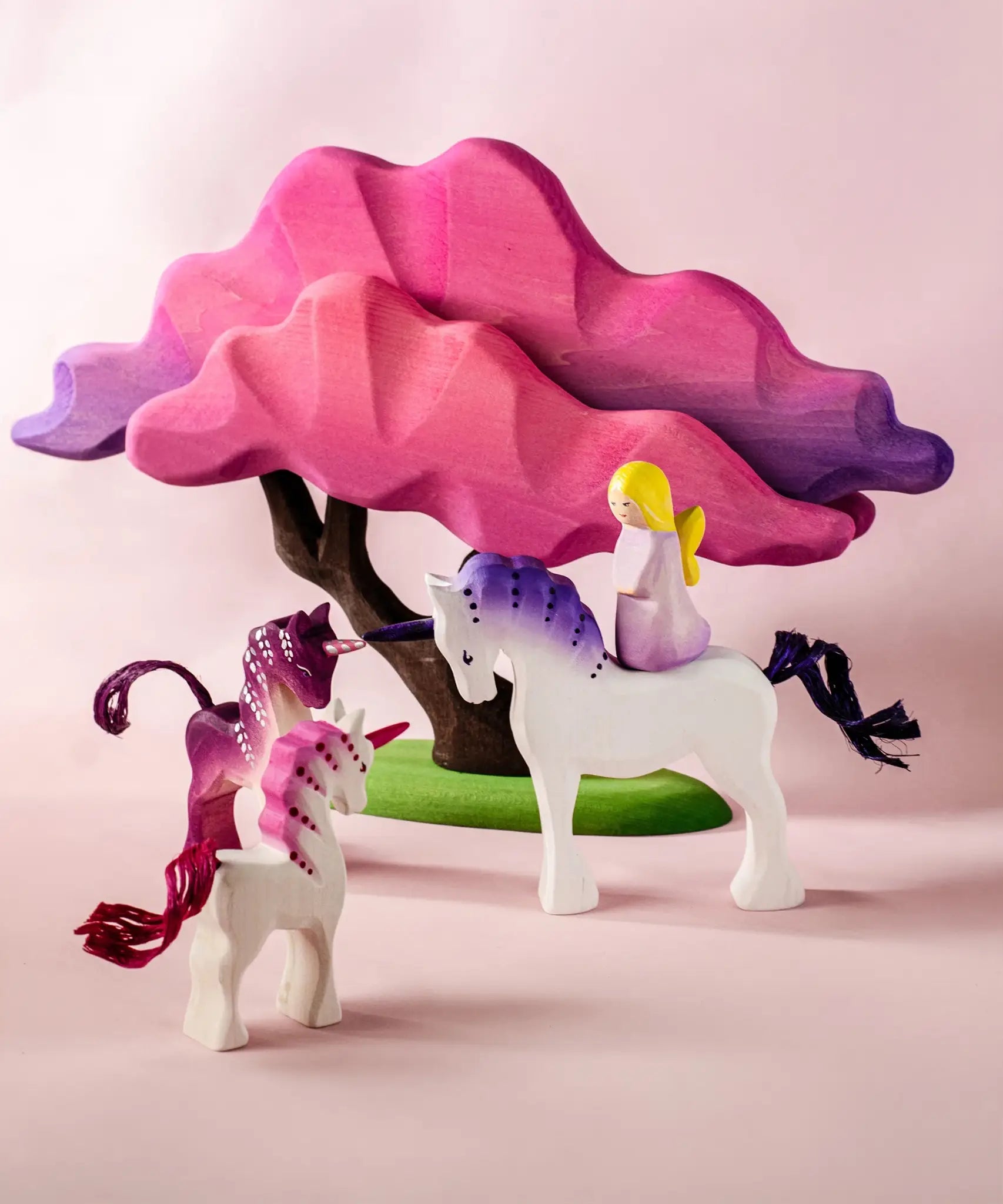 Bumbu wooden pink fairy figure standing on top of a white unicorn next to small pink unicorns and blossom tree figures