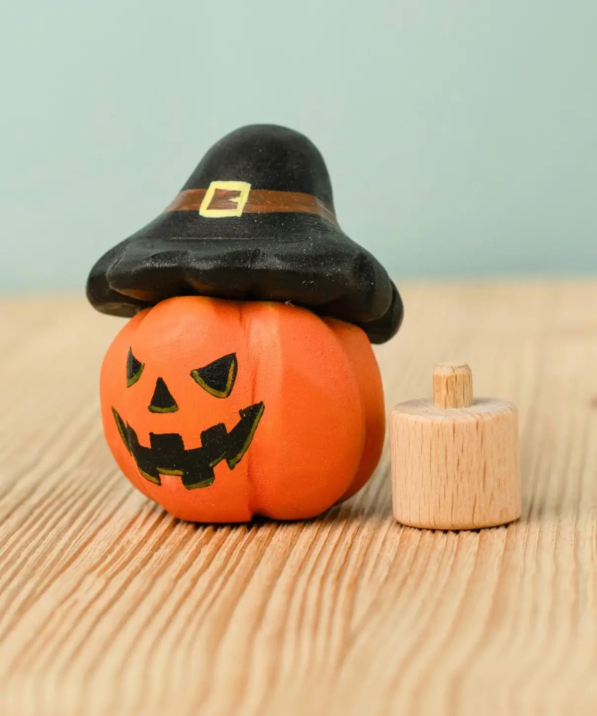 Bumbu handcrafted wooden magic pumpkin decorative figure wearing a black hat next to a small display peg