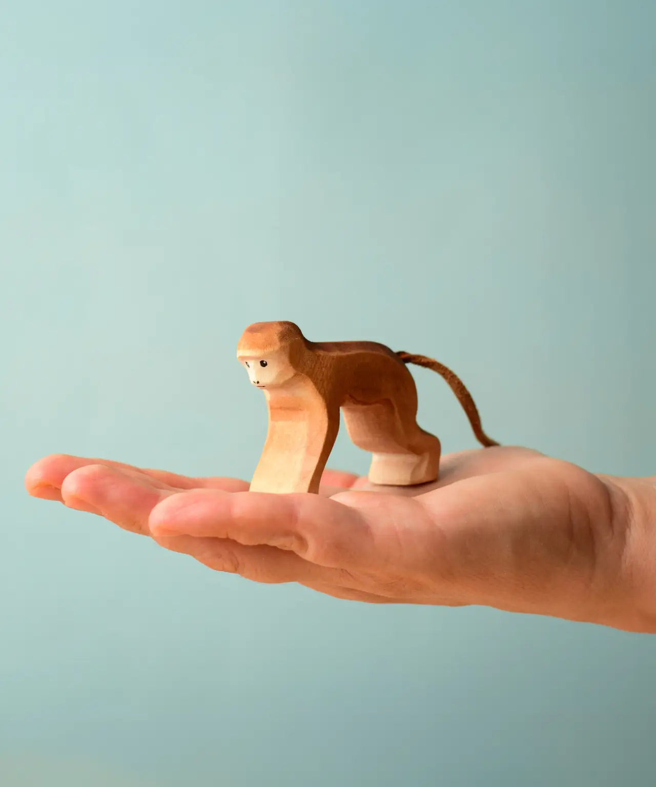 Adult hand holding a Bumbu toys handcrafted wooden brown monkey  showing scale