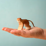 Adult hand holding a Bumbu toys handcrafted wooden brown monkey  showing scale