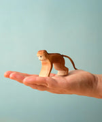 Adult hand holding a Bumbu toys handcrafted wooden brown monkey  showing scale