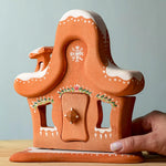 A hand next to the Bumbu wooden gingerbread house for size .