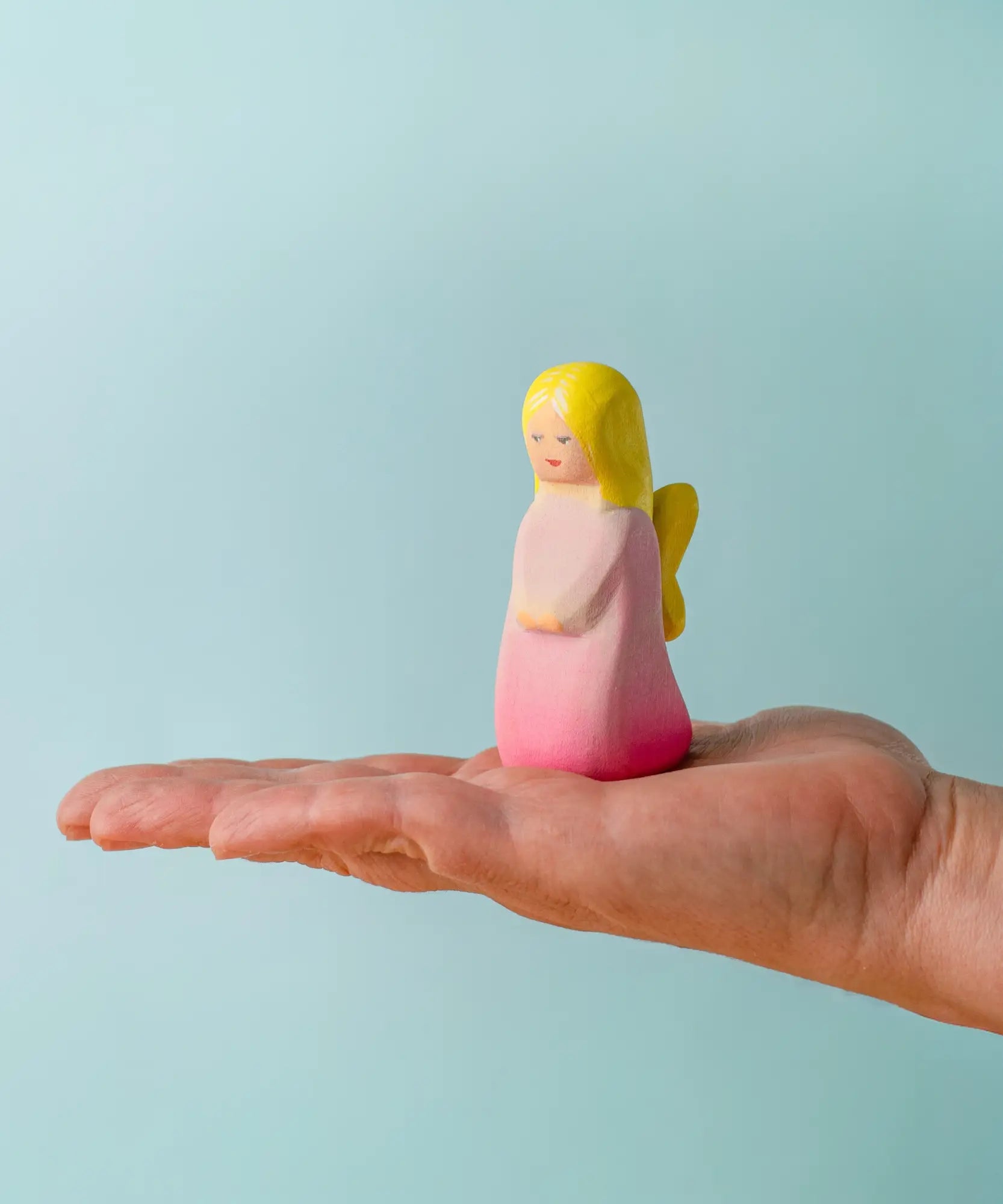 Adult hand holding the Bumbu wooden pink fairy figure showing scale