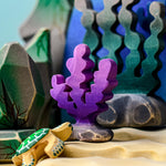 A purple Bumbu seaweed figure placed in a samll world play set up surrounded by other varieties of seaweed and rocks