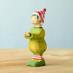 A wooden Bumbu Santas elf wearing a red and white striped hat and a green outfit with its hands holding out to carry presents.