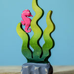 A bumbu wooden seahorse figure perched on green Bumbu sugar kelp seaweed