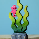 A bumbu wooden seahorse figure perched on green Bumbu sugar kelp seaweed