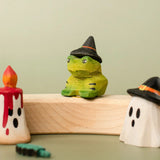 Bumbu handcrafted wooden spell green frog decorative figure displayed on a celebration ring next to a red candle and ghost wizard figure