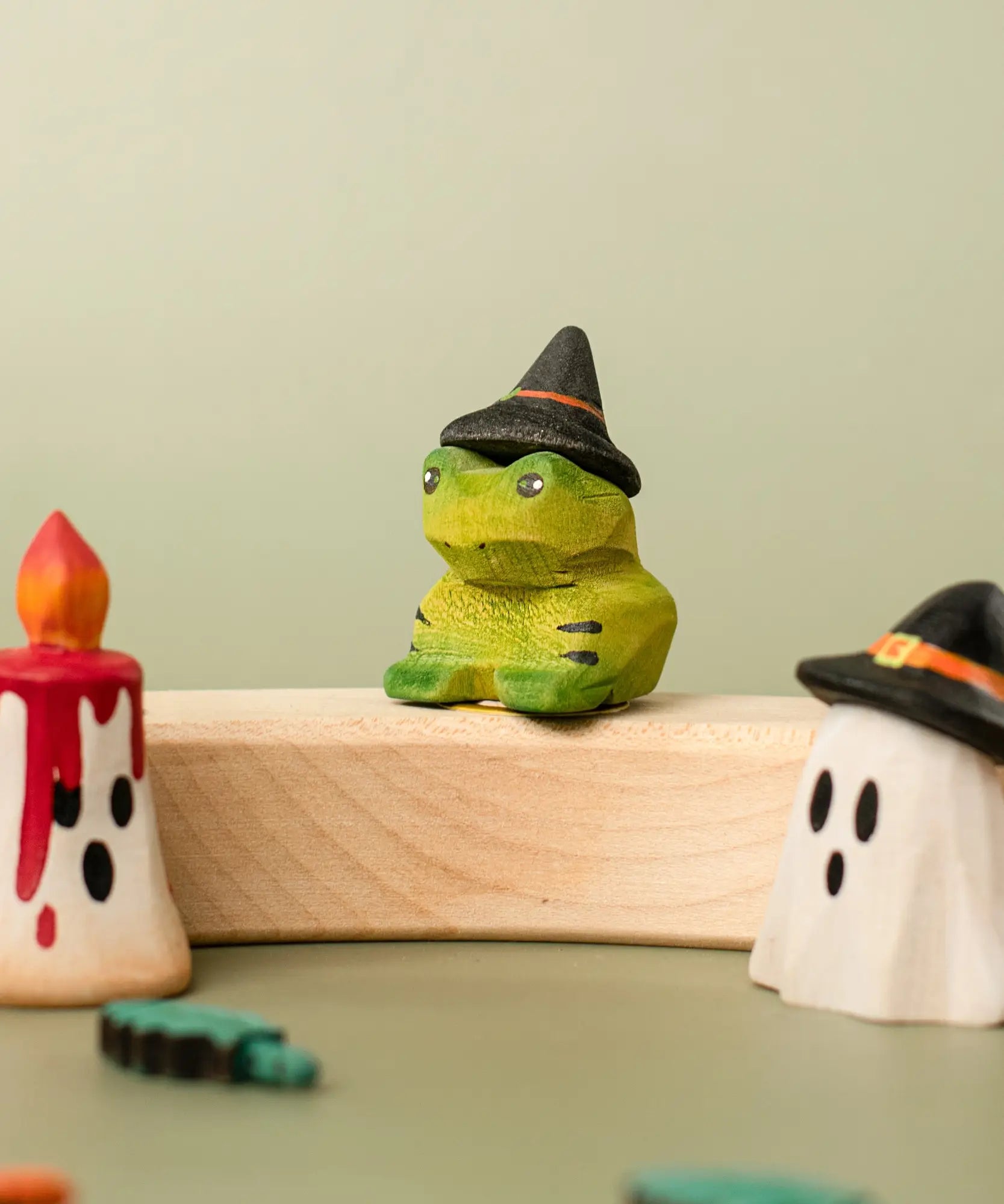 Bumbu handcrafted wooden spell green frog decorative figure displayed on a celebration ring next to a red candle and ghost wizard figure