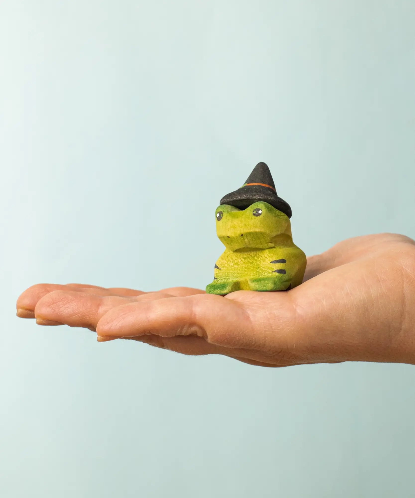 Bumbu handcrafted wooden spell green frog decorative figure on a adult hand showing scale