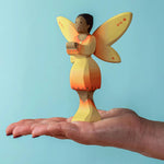 An adult balancing a Bumbu Wooden Sunflower Fairy on their hand against a blue background.