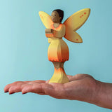 An adult balancing a Bumbu Wooden Sunflower Fairy on their hand against a blue background.