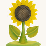 Bumbu Large Wooden Sunflower, Hand Crafted and Hand Painted. A Large yellow Sunflower with green stalk and leaves, on a green wooden base being held in a hand. On a blue background