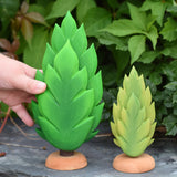 A hand reaching out for the large thuja wooden tree that has been placed on a slate surface outdoors. There is a small thuja tree next to it. These expertly hand crafted items are part of a large range of wooden toys available here at Babipur. 