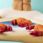 Three hand carved wooden red crab toys from Bumbu, posed on a toy rockpool