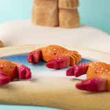 Three hand carved wooden red crab toys from Bumbu, posed on a toy rockpool