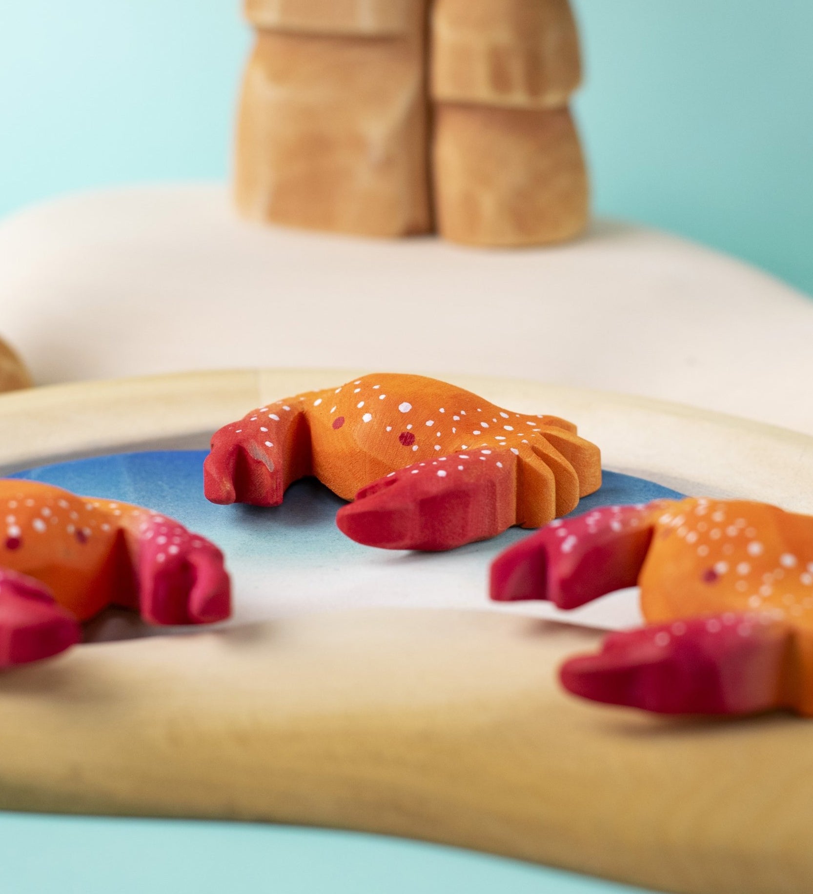 Three hand carved wooden red crab toys from Bumbu, posed on a toy rockpool