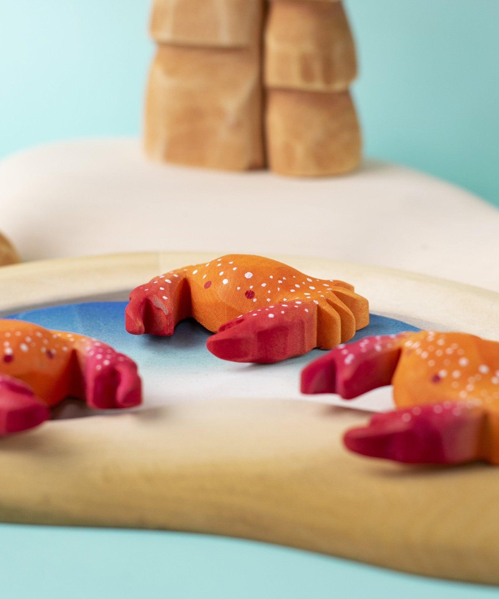 Three hand carved wooden red crab toys from Bumbu, posed on a toy rockpool