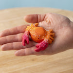 A hand holding the Bumbu handmade wooden red crab toy for size reference