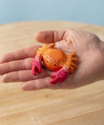 A hand holding the Bumbu handmade wooden red crab toy for size reference