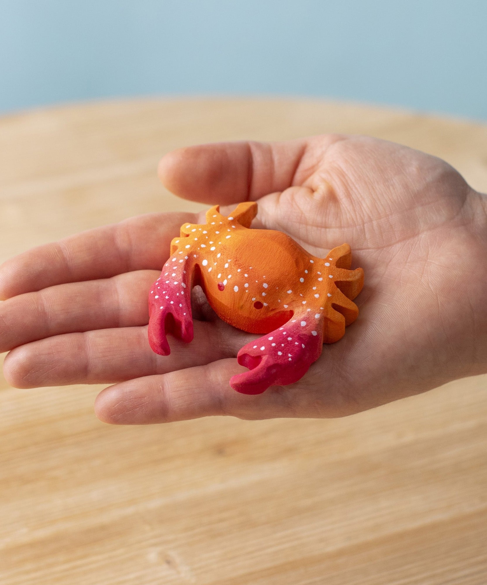 A hand holding the Bumbu handmade wooden red crab toy for size reference