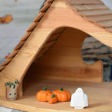 A Bumbu white ghost figure placed next to three wooden pumpkins in an Ostheimer wooden cottage. 