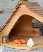 A Bumbu white ghost figure placed next to three wooden pumpkins in an Ostheimer wooden cottage. 