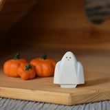 A close up of a Bumbu white ghost figure placed next to three wooden pumpkins in an Ostheimer wooden cottage. 