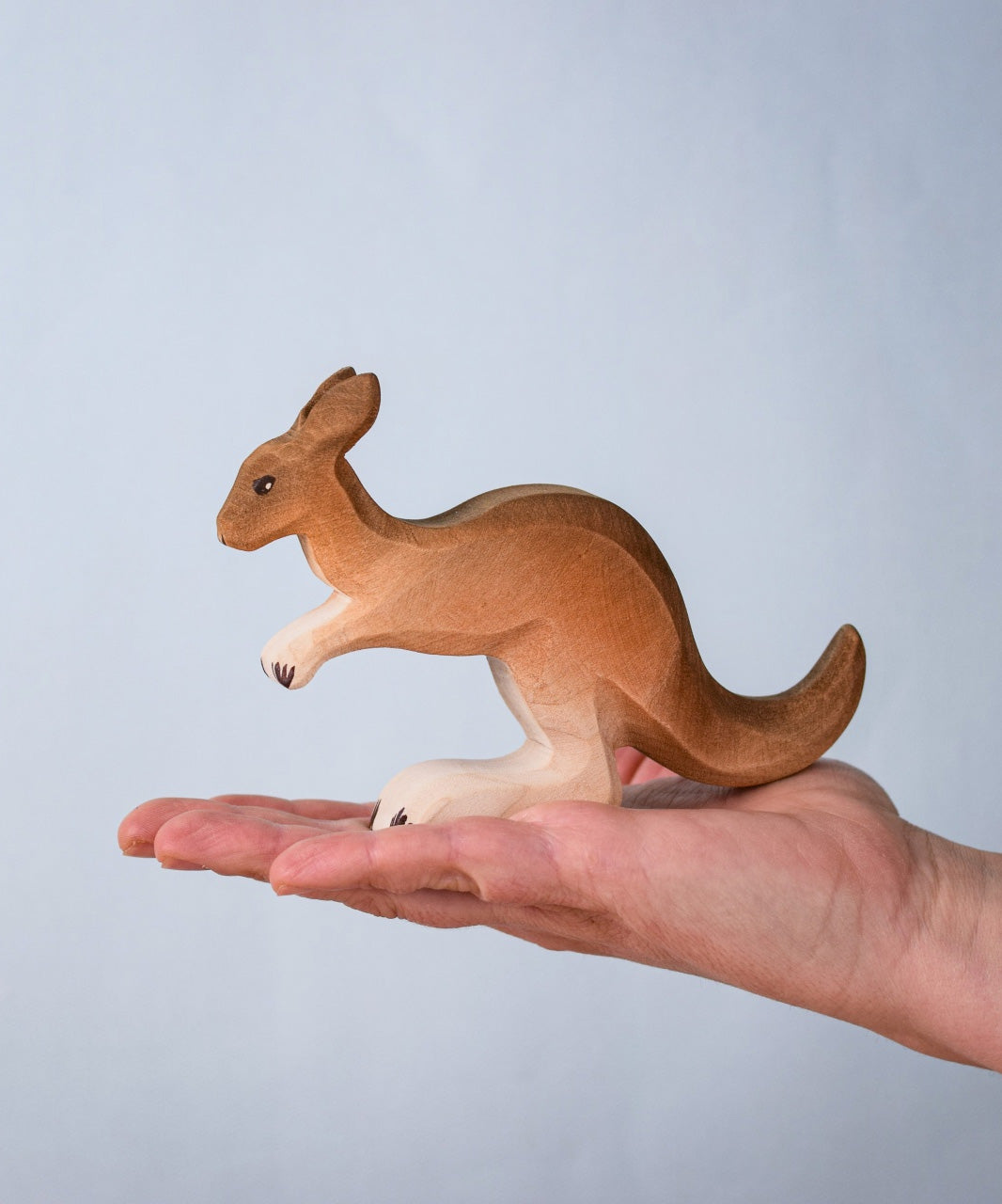 The Bumbu wooden toy kangaroo figure, held on a stretched palm to show its comparative size.