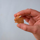 A hand holding The Bumbu Toys wooden baby brown rabbit, sat in a perching position, for size reference