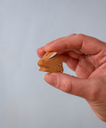 A hand holding The Bumbu Toys wooden baby brown rabbit, sat in a perching position, for size reference